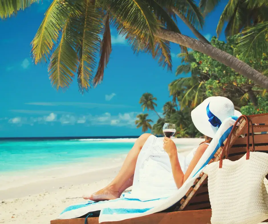 A mom lounging on the beach with a glass of wine, gazing at the beautiful blue ocean, stress-free thanks to planning in advance.