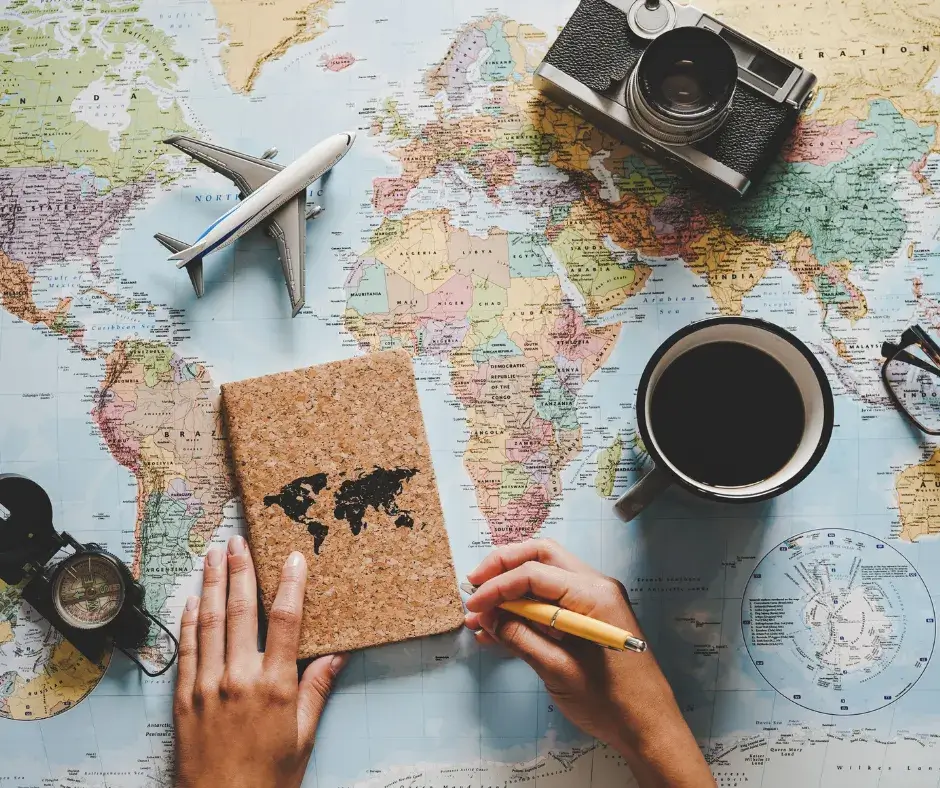 A map, travel planning journal, camera, and a cup of coffee on a table as a parent prepares for the family's next adventure, emphasizing the importance of planning travel ahead of time.