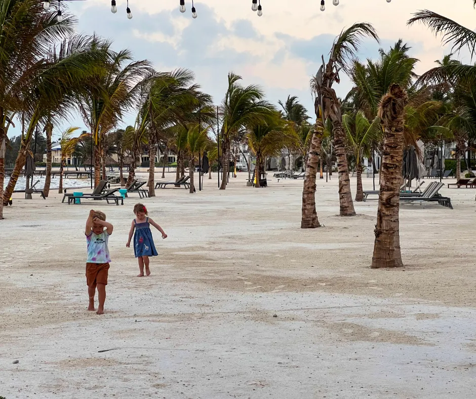 Belize beach hotel grounds with palm trees and lounge chairs; two kids walk on white sand — Beach & Jungle Stays We Love With Kids