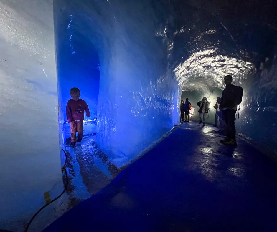 Blue ice tunnel inside the Chamonix ice hotel in the French Alps, with visitors walking along a glossy blue ice corridor.