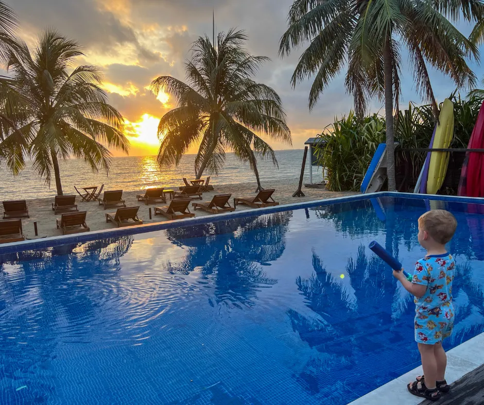 Belize boutique hotel pool at sunset, palms, loungers, child nearby